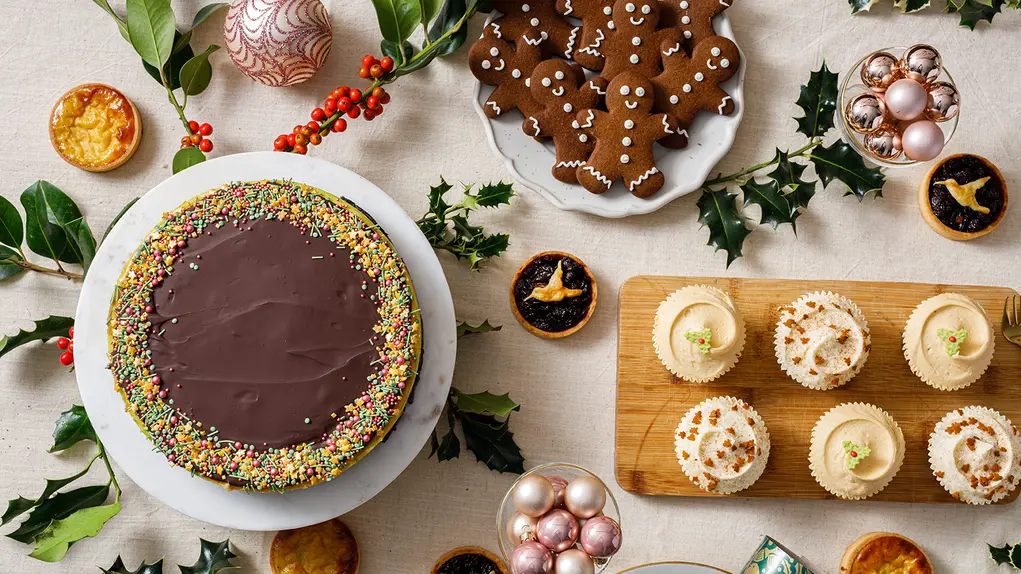 Festive Christmas treats on a table including chocolate cake, gingerbread cookies, and mince pies