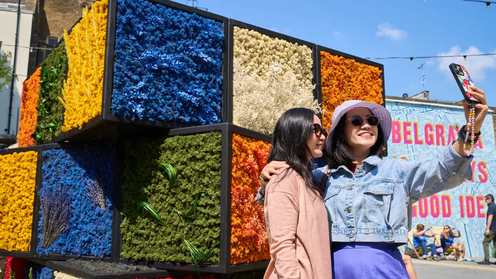 Two women take a selfie in front of a Rubik's cube flower display