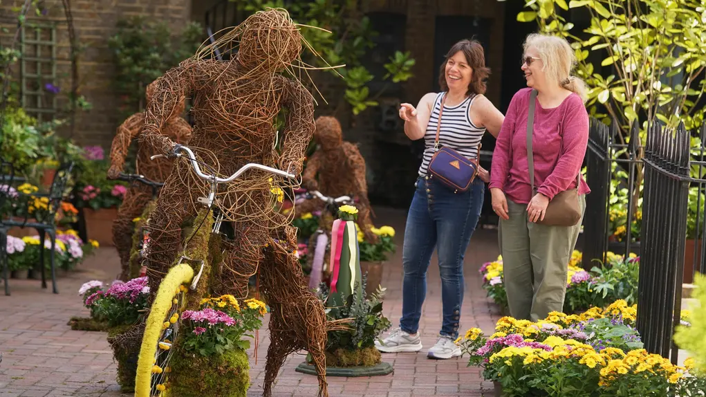A plant display of a person riding a bicycle while two people look on
