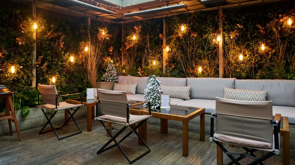 A terrace with fairy lights, chairs and tables, and Christmas tree table decorations 