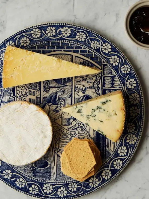 Assorted gourmet cheeses and crackers on a vintage blue-patterned plate
