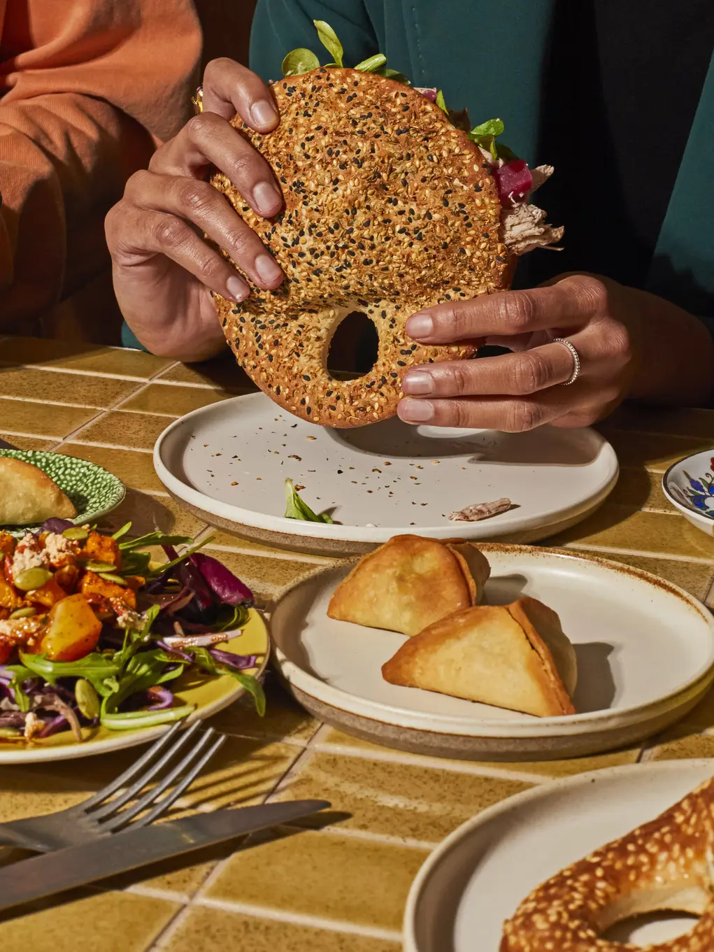 Showing hands holding a sandwich and other plates of salad and bread