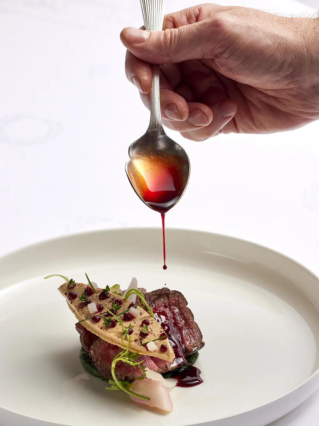 A small plate of meat with a hand holding a spoon with syrup over the top of it
