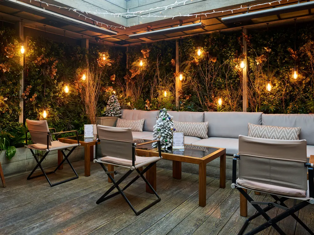 A terrace with fairy lights, chairs and tables, and Christmas tree table decorations 